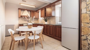 Eine Küche mit Holzschränken, einem weißen Kühlschrank, einem Esstisch mit Stühlen und einer gefliesten Spritzschutzleiste.