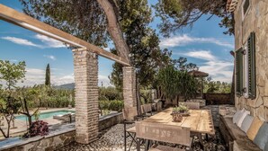 Eine Terrasse im Freien mit Steinboden, Holztisch, Korbstühlen und einer Steinmauer.