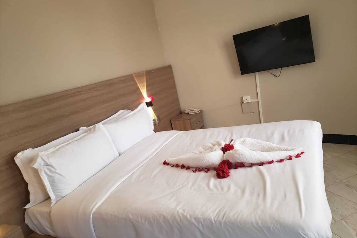 Habitación de hotel con una cama bien hecha, un televisor de pantalla plana en la pared y una mesita de noche con un teléfono.