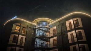 Um hotel com vários andares, fachada curva, varandas e uma escadaria espiral central.