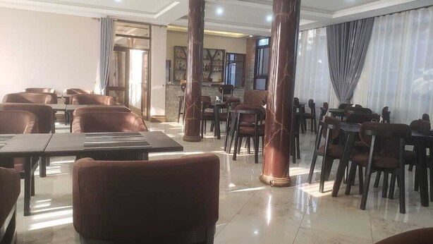 Um restaurante espaçoso com tetos altos, colunas de mármore e assentos de couro. Mesas dispostas para refeições.