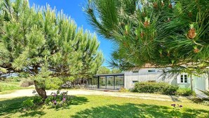 Una casa moderna con un invernadero de vidrio, rodeada de un césped cuidado y pinos.