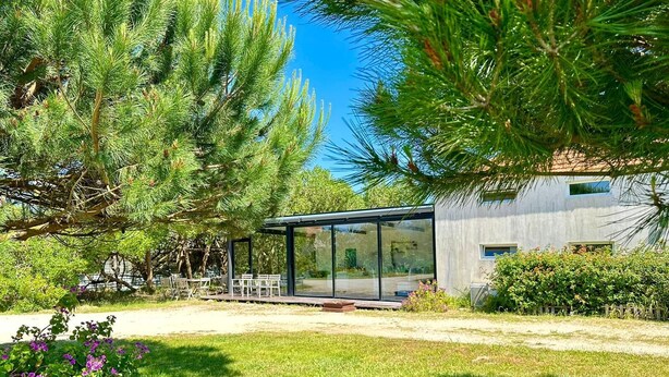Una casa moderna con un invernadero de vidrio, rodeada de abundante vegetación y un césped cuidado.