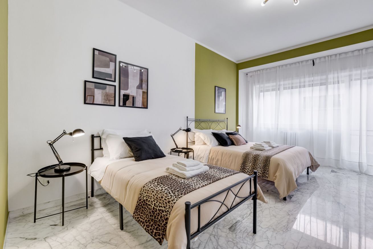 Hotellihuone, jossa on kaksi sänkyä, marmorilattia, vihreä tehosteseinä ja taideteoksia seinällä.