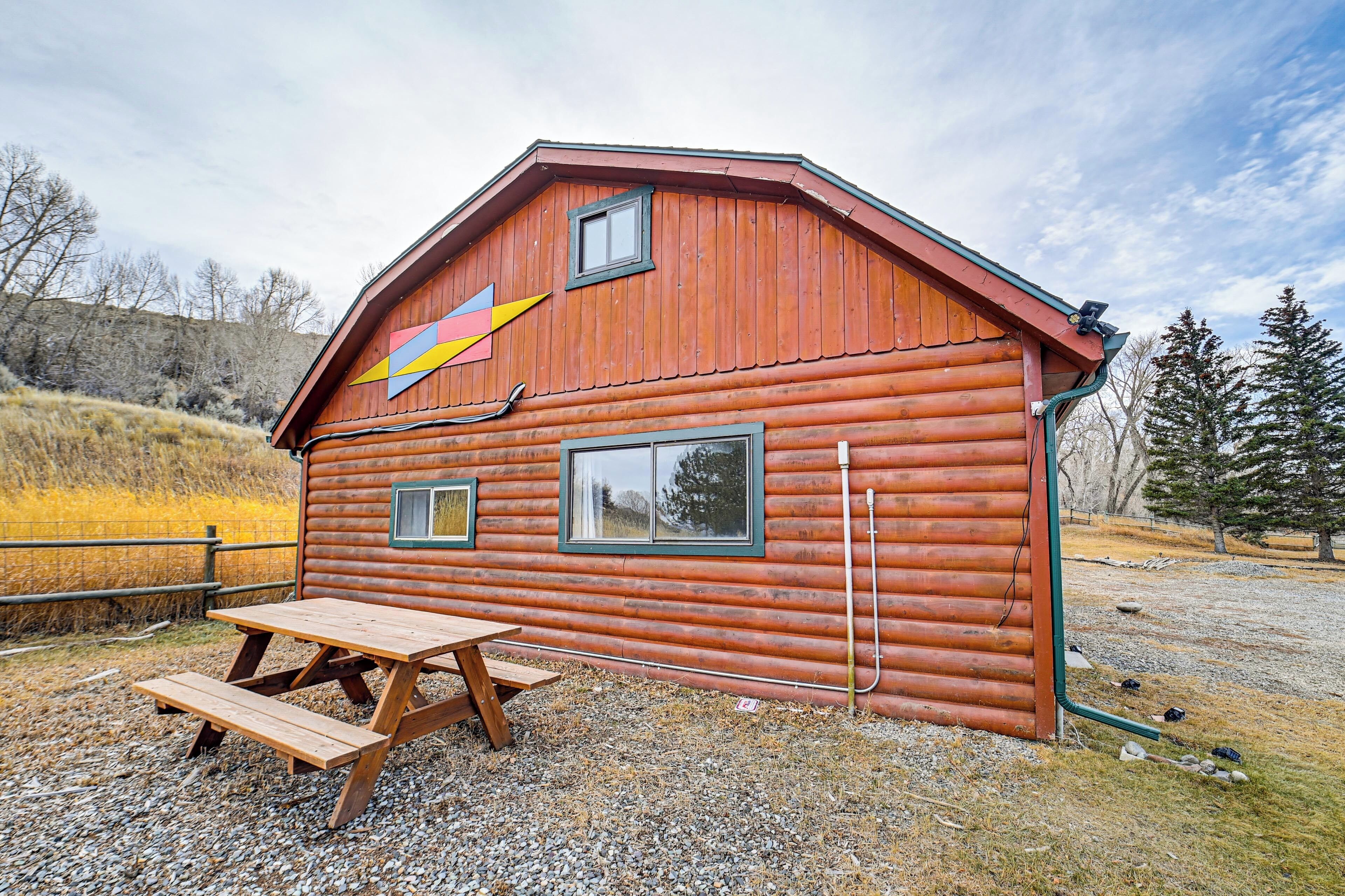 A rustic wooden cabin with a picnic table, a colorful arrow decoration, and a small window.