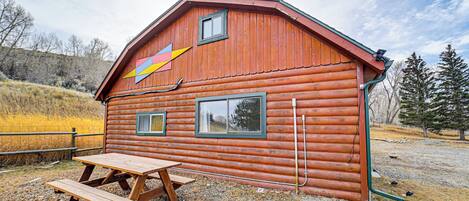 A rustic wooden cabin with a picnic table, a colorful arrow decoration, and a small window.
