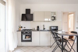 A modern kitchen with a gas stove, oven, microwave, and a dining area with a table and chairs. - By The Lake Motta Avenue - Park and Lake (Desenzano del Garda)