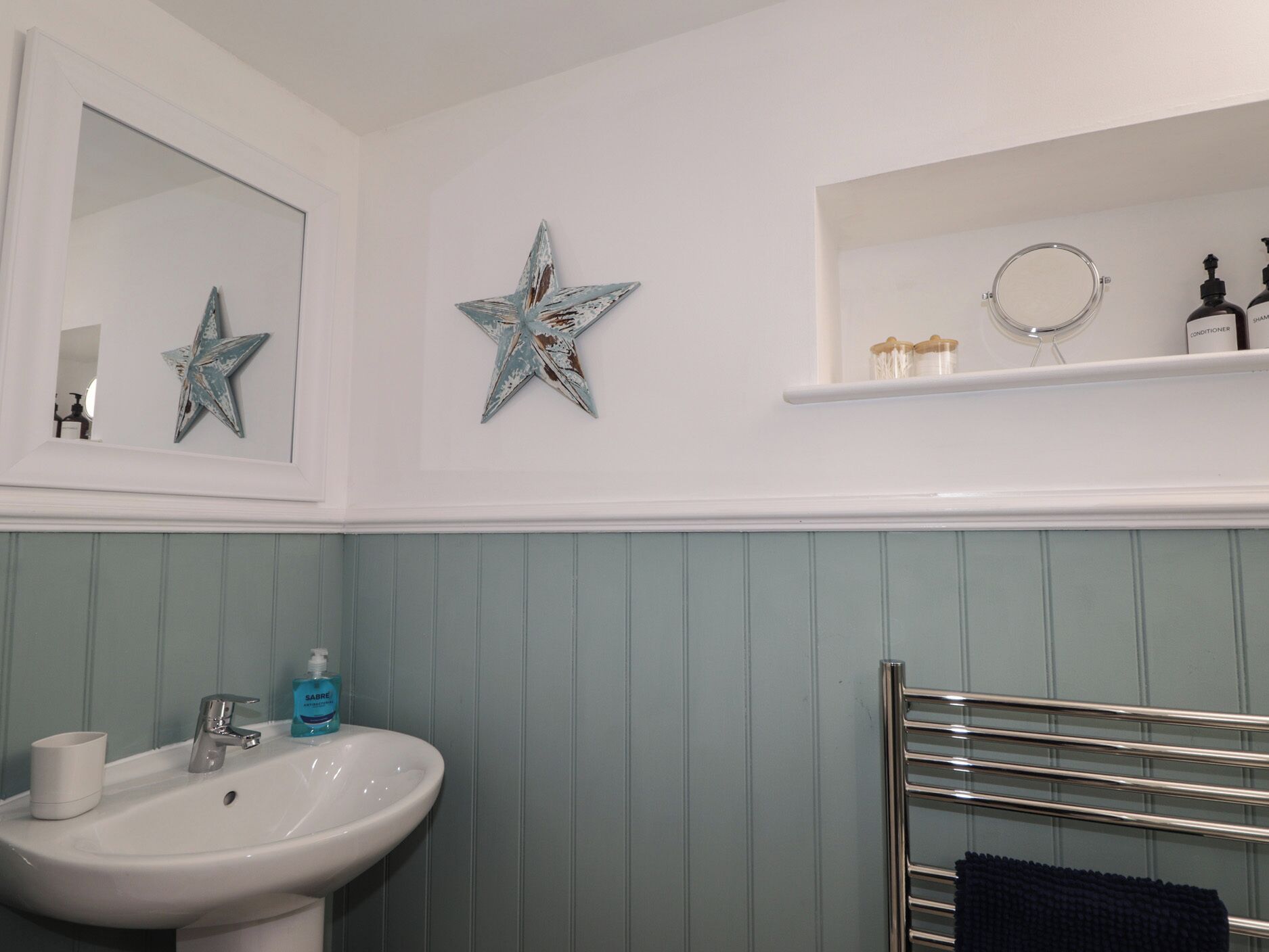 A bathroom with a white sink, two star-shaped wall decorations, a mirror, and a shelf with toiletries.