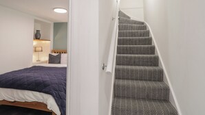 Une chambre à coucher avec un lit, une table de chevet, une lampe et une vue sur un escalier.