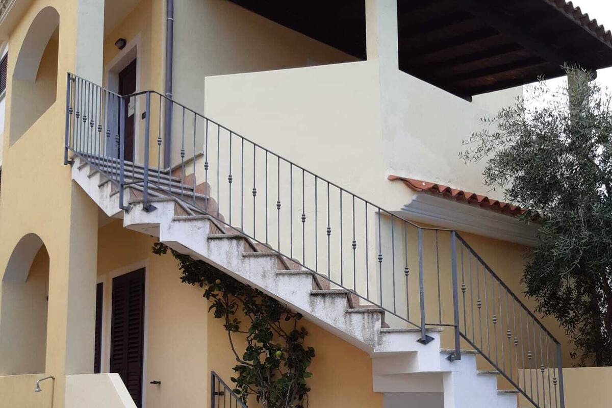 A two-story building with a stone-paved courtyard, a staircase with metal railings, and a covered area with a tiled roof.