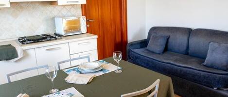 A compact living space with a dining table set for two, a sofa, and a kitchenette with a stove and toaster.