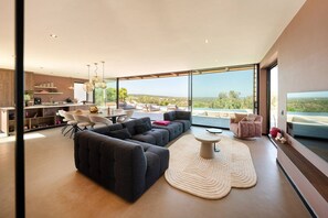 A modern living room with a sectional sofa, a round coffee table, and a view of the outdoors. - Villa Maggio - Luxury modern villa with private pool  (Carovigno)