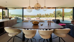 Uma sala de jantar moderna com uma mesa grande, seis cadeiras e vista para o exterior.
