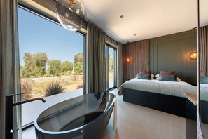 A modern bedroom with a large window, a bathtub, and a bed with multiple pillows. - Villa Maggio - Luxury modern villa with private pool  (Carovigno)