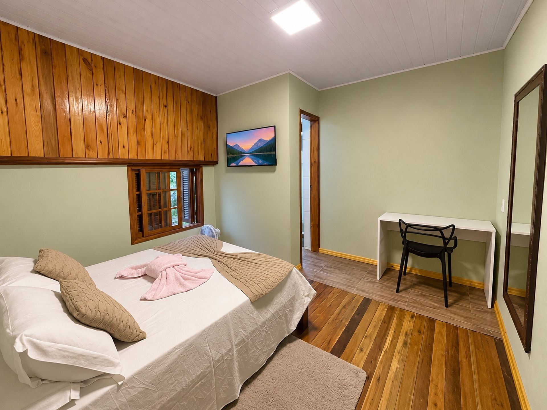 Een slaapkamer met een bed, een bureau, een stoel, een raam en een schilderij aan de muur.