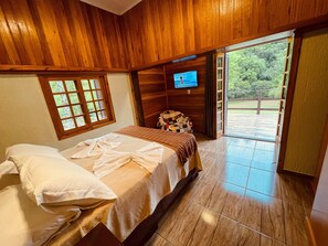 A wooden room with a bed, a television, and a view of the outdoors. - Sítio Refúgio da Serra Canela (Canela)