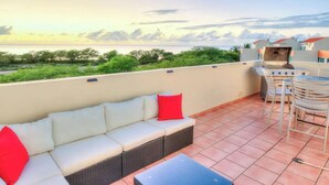 Eine Dachterrasse mit einer Couch, Stühlen, einem Tisch und einem Grill.