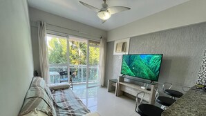 A modern living room with a sofa, a TV, a bar area, and a balcony with a view of greenery. - Porto Real Resort - Leisure and Fun (Mangaratiba)