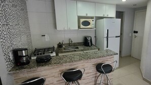 A kitchen with a microwave, refrigerator, coffee maker, and gas stove. There are two bar stools. - Porto Real Resort - Leisure and Fun (Mangaratiba)