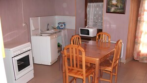 Une cuisine compacte équipée d’une cuisinière, d’un four à micro-ondes et d’un évier. On y trouve également une table à manger avec quatre chaises.