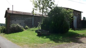 Un paysage rural avec un bâtiment en pierre, un champ verdoyant et un chemin de terre.