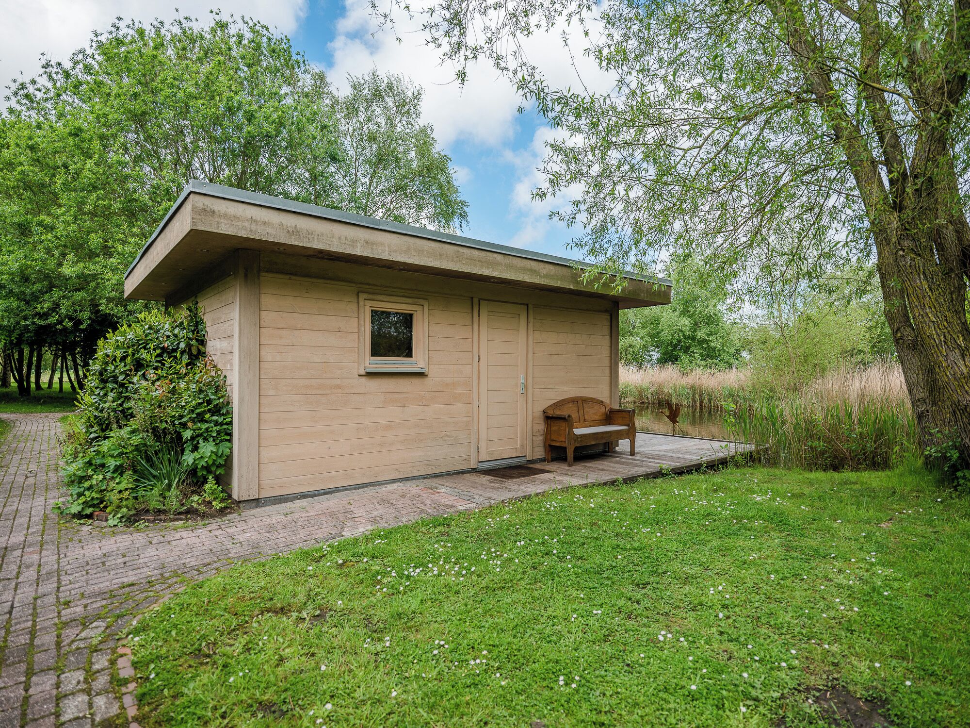 A small wooden cabin with a bench outside, surrounded by greenery and a clear sky.