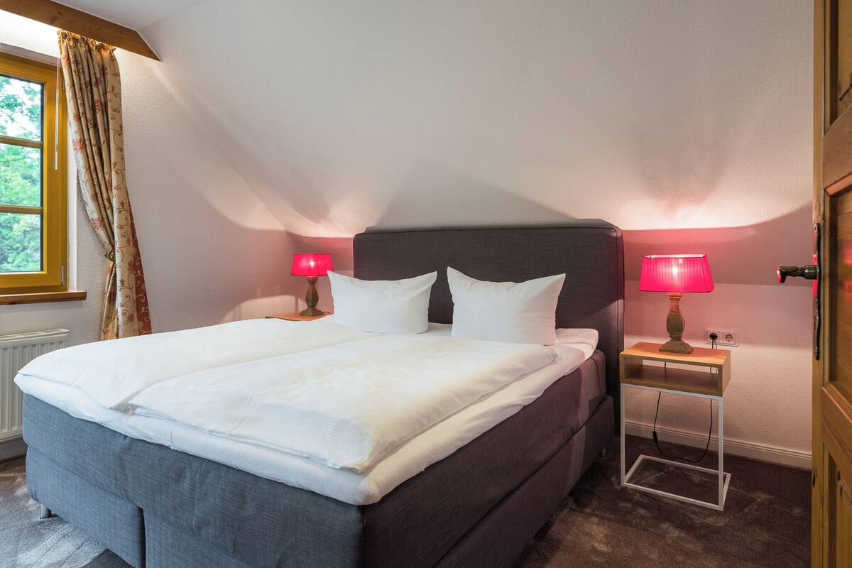 A neatly made bed with white linens, a dark headboard, and two bedside tables with red lamps.