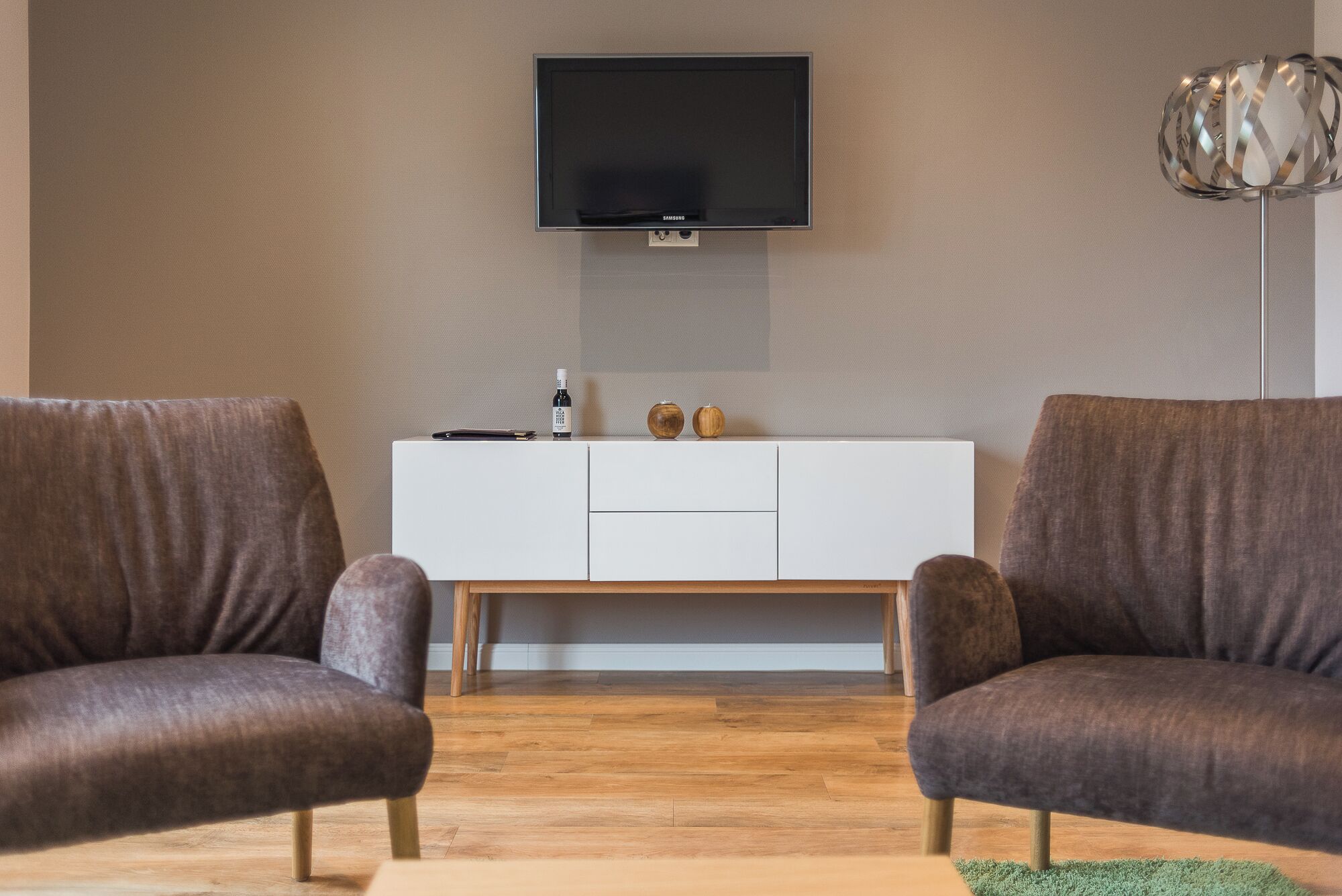 Ein modernes Wohnzimmer mit zwei Sesseln, einem weißen Konsolentisch und einem flachbildfernseher an der Wand.