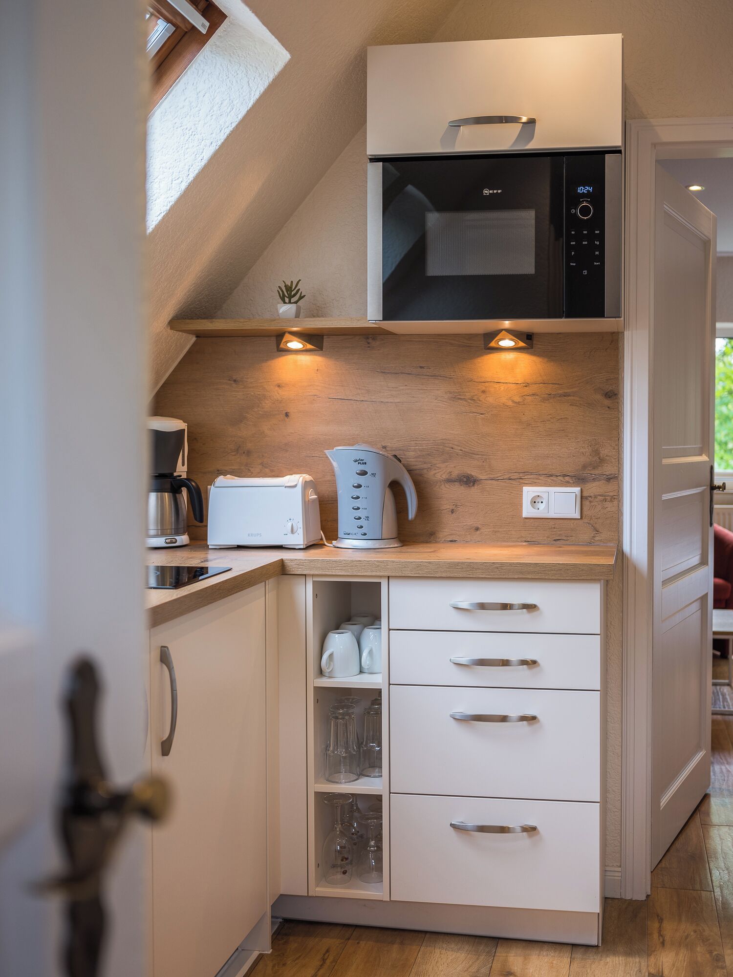 Une cuisine compacte équipée d’un four à micro-ondes, d’un grille-pain et d’une bouilloire, le tout posé sur un plan de travail en bois.