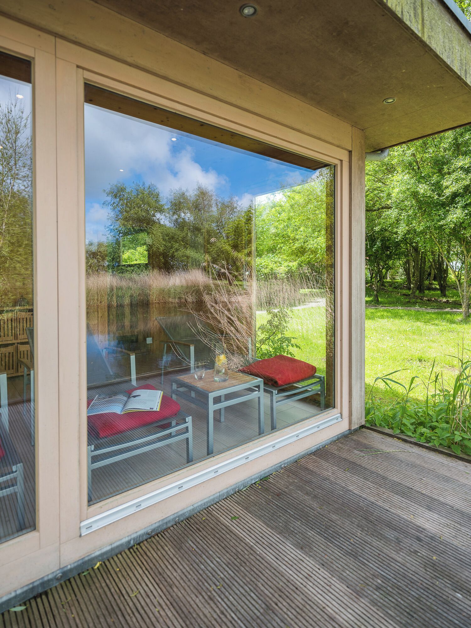 A modern outdoor seating area with a glass enclosure, a wooden deck, and a view of a natural landscape.