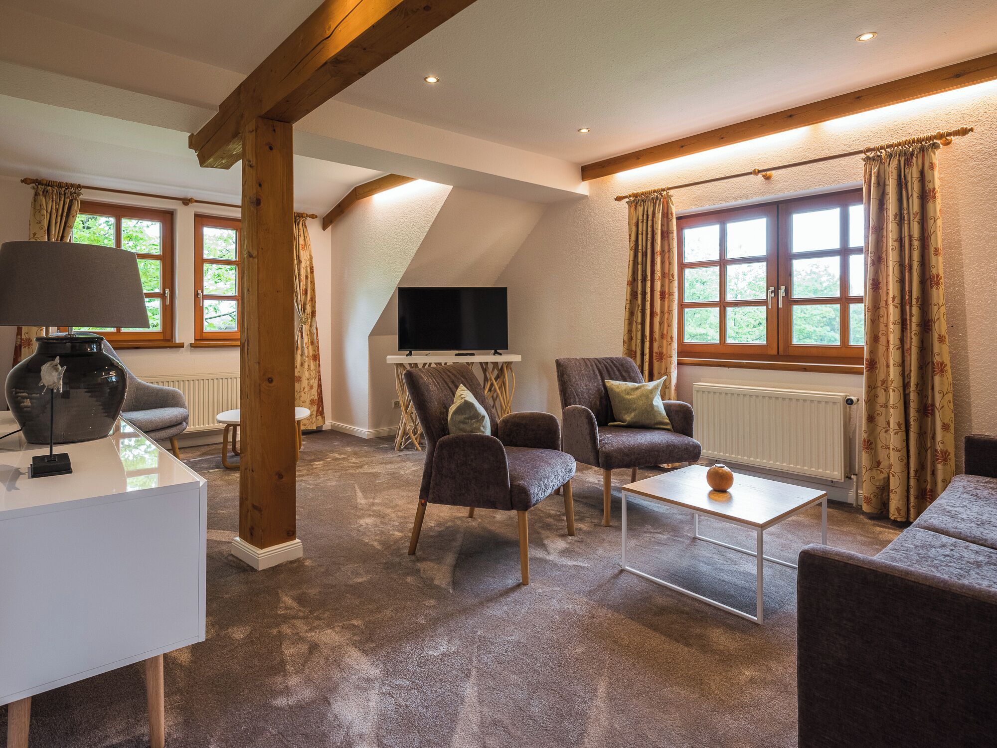 A cozy living room with a TV, comfortable seating, and large windows.
