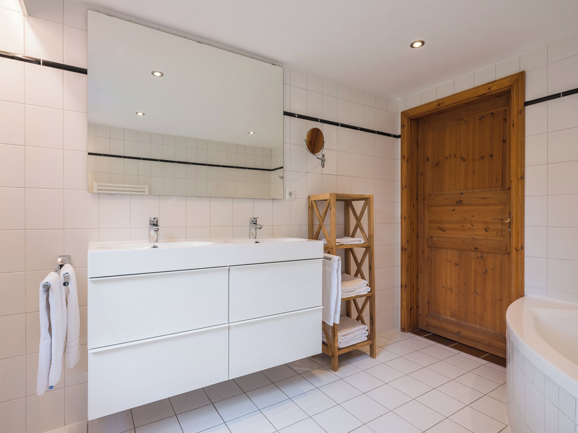 A modern bathroom with a large mirror, a wooden door, and a white bathtub.
