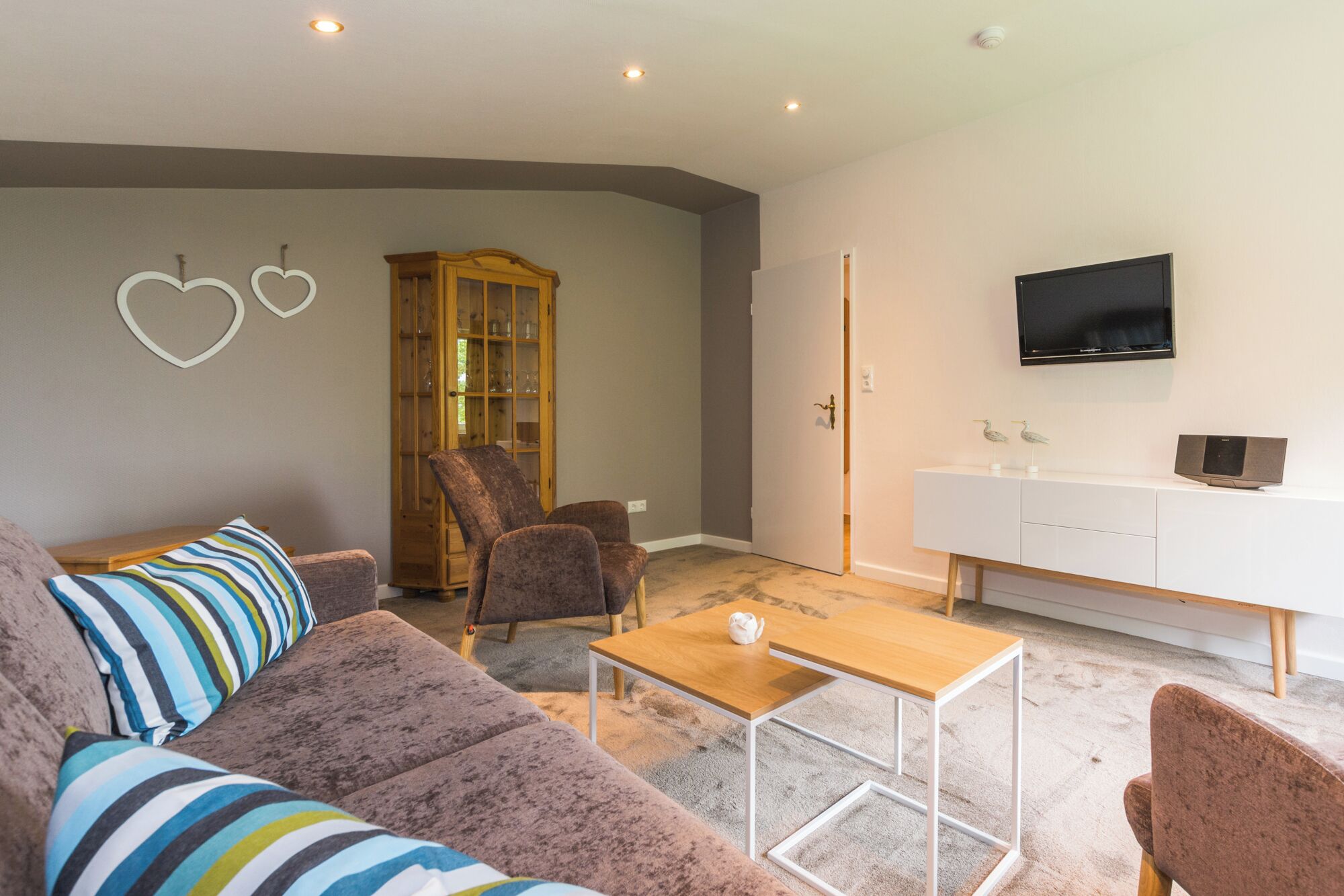 Una sala de estar moderna con un sofá, sillas, una mesa de centro, un aparador y un televisor montado en la pared.