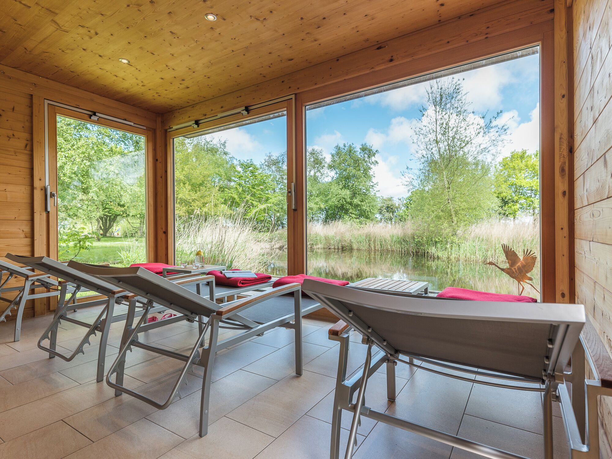 Une pièce dotée de grandes fenêtres, offrant une vue sur un lac, et comprenant une table recouverte d’une nappe rouge.