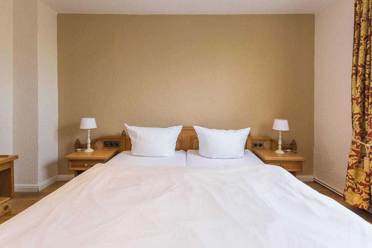 A hotel room with a large bed, two bedside tables with lamps, and a plain wall.