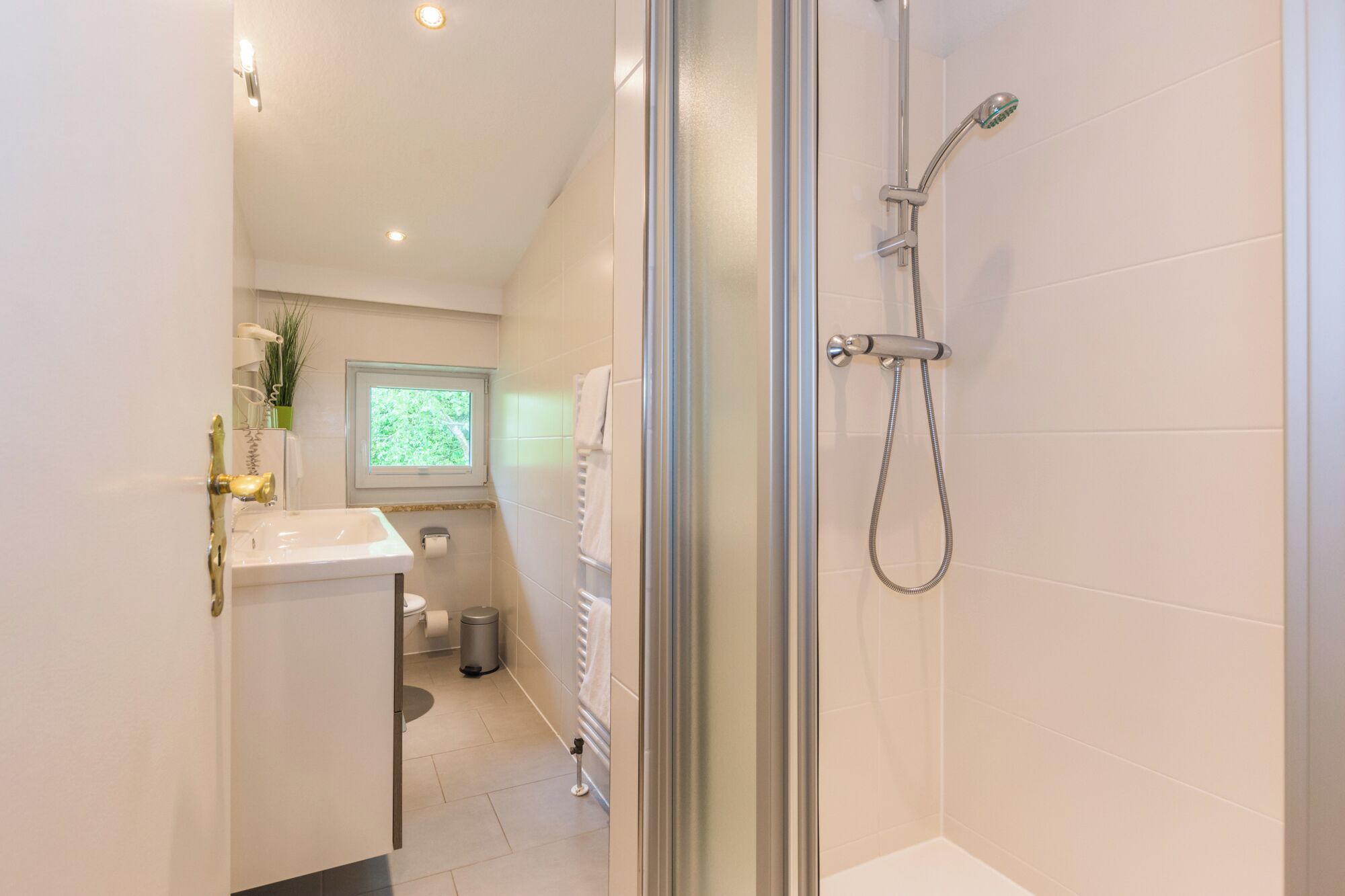 A modern bathroom with a glass shower enclosure, a white sink, and a window providing natural light.