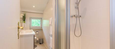 A modern bathroom with a glass shower enclosure, a white sink, and a window providing natural light.
