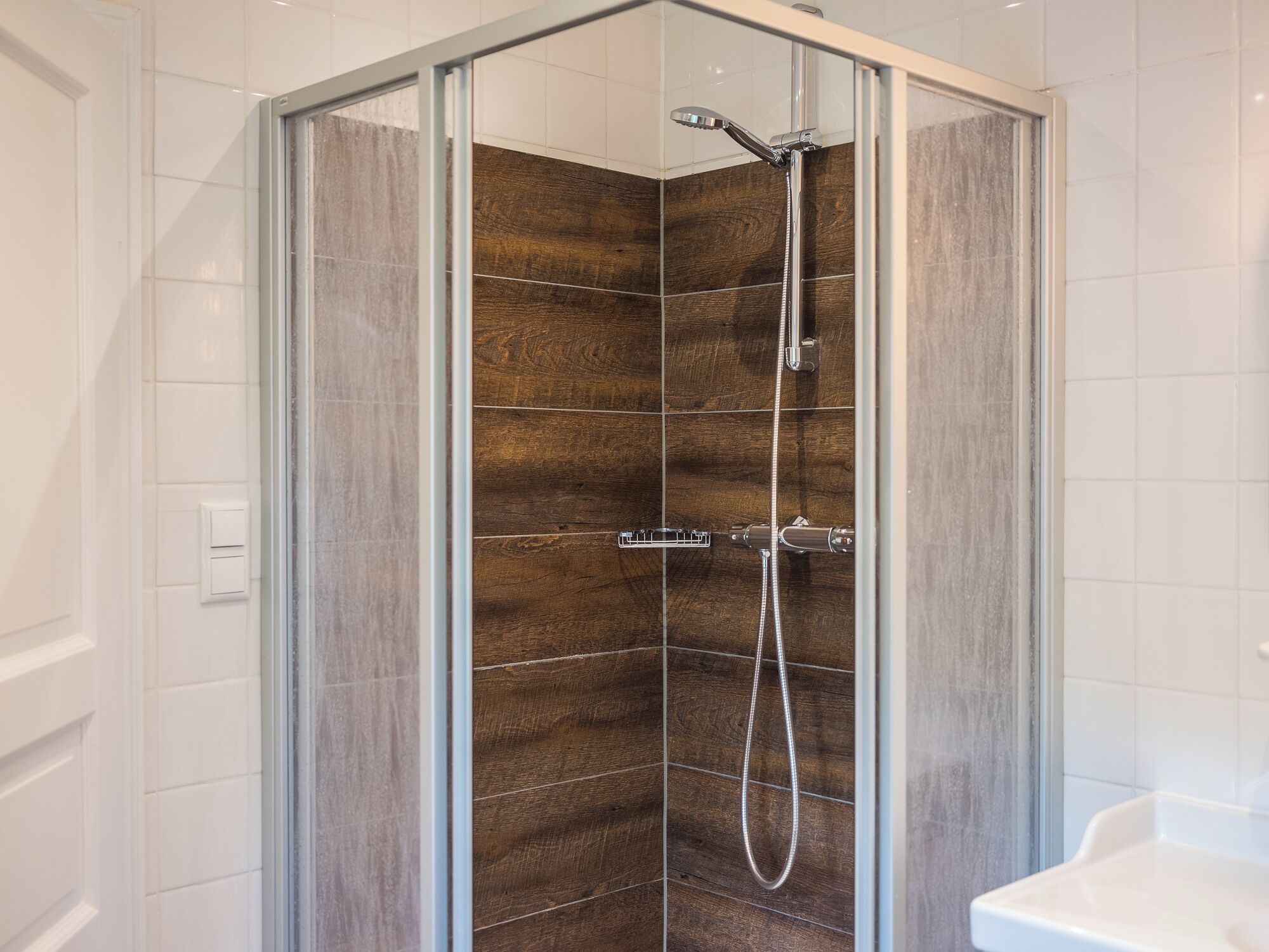 Une douche fermée par des parois en verre, avec un mur en panneaux de bois, une douchette à main et un robinet mural.
