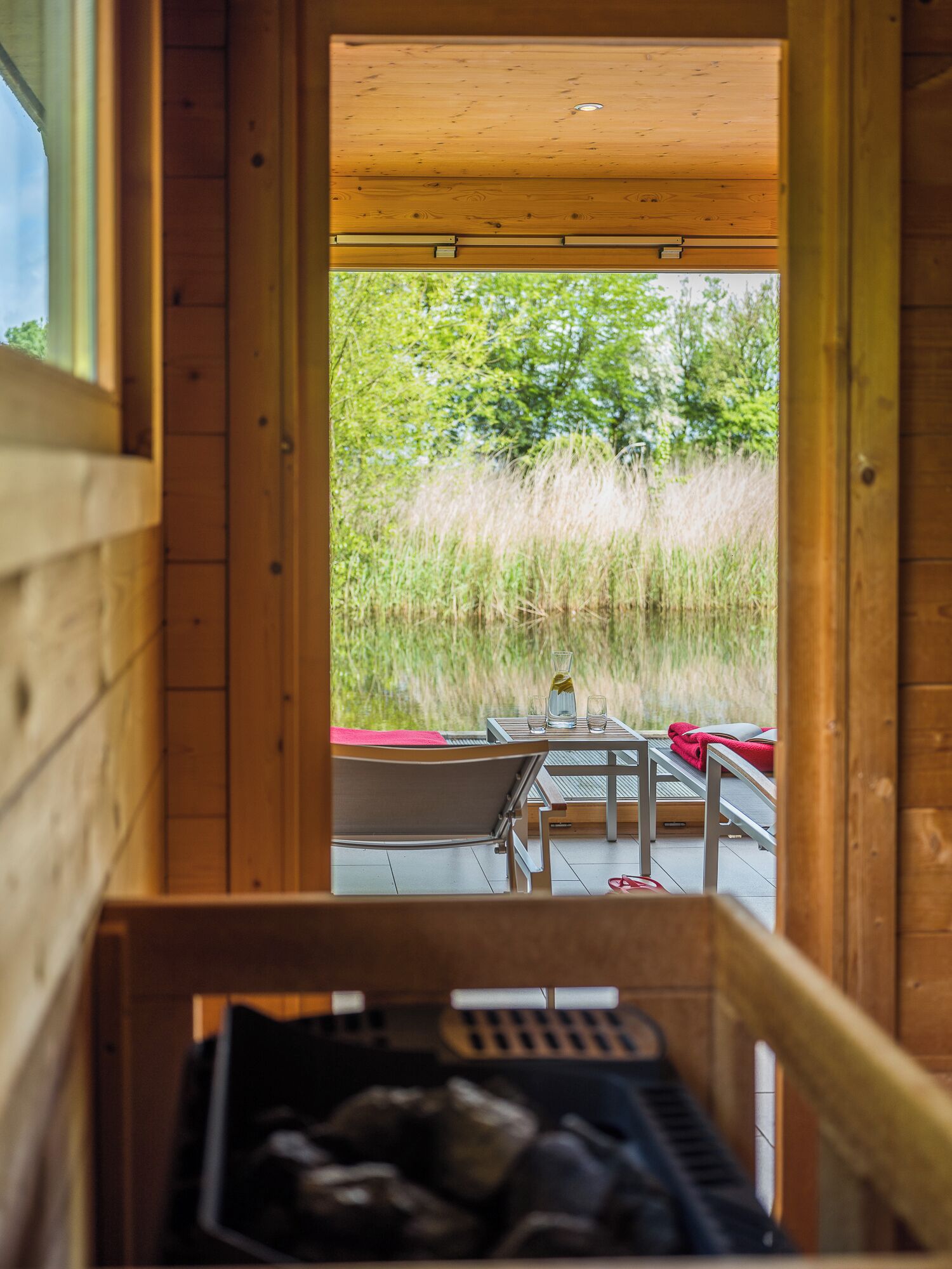 A wooden cabin with a view of tall grass and trees. Inside, there is a table with chairs and a red towel.