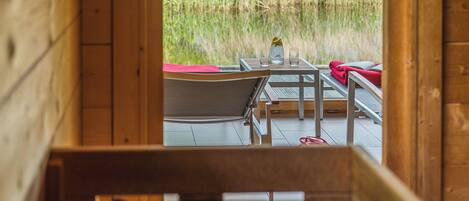 A wooden cabin with a view of tall grass and trees. Inside, there is a table with chairs and a red towel.