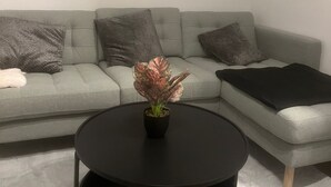 Una sala de estar moderna con un sofá seccional gris, una mesa de centro negra y un cuadro enmarcado con un paisaje costero en la pared.