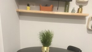 Una mesa redonda de comedor con cuatro sillas, una planta en maceta y una repisa superior con adornos.