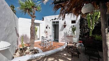 Un patio con un muro blanco, una puerta, una mesa con sillas y un banco.