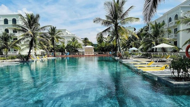 A large swimming pool with palm trees and lounge chairs, surrounded by white buildings with arched windows. - MK Hotel Phu Quoc (Phu Quoc)
