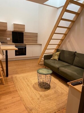 A modern living space with a kitchen, a green sofa, a small round table, and a wooden ladder. - HÉBERGEMENT ORNANO BORDEAUX (Bordeaux)