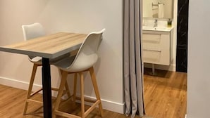 Una zona d'esmorzar moderna amb una taula de fusta i cadires blanques, un terra de fusta i un bany visible per una porta.