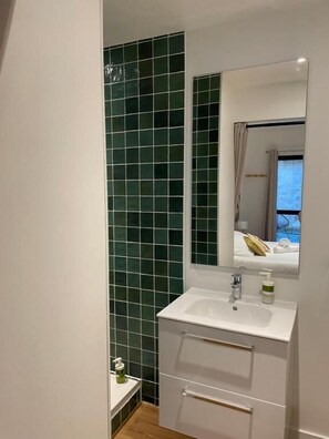 A modern bathroom with a white sink, mirror, and green-tiled walls. - HÉBERGEMENT ORNANO BORDEAUX (Bordeaux)