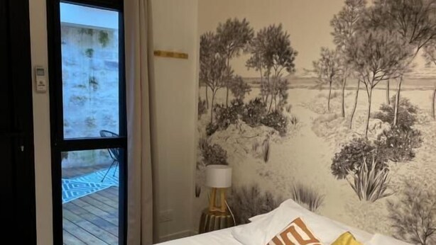 Una habitació d'hotel amb un llit, un quadre amb arbres, una finestra i una porta.