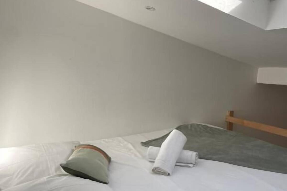 Un dormitorio con tragaluces, una cama con ropa blanca, una almohada y una toalla enrollada.