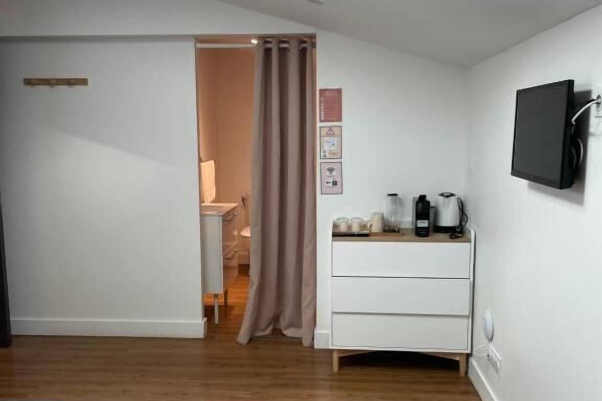 Un dormitorio con una cama, una mesita de noche con televisor y una ventana con cortinas.
